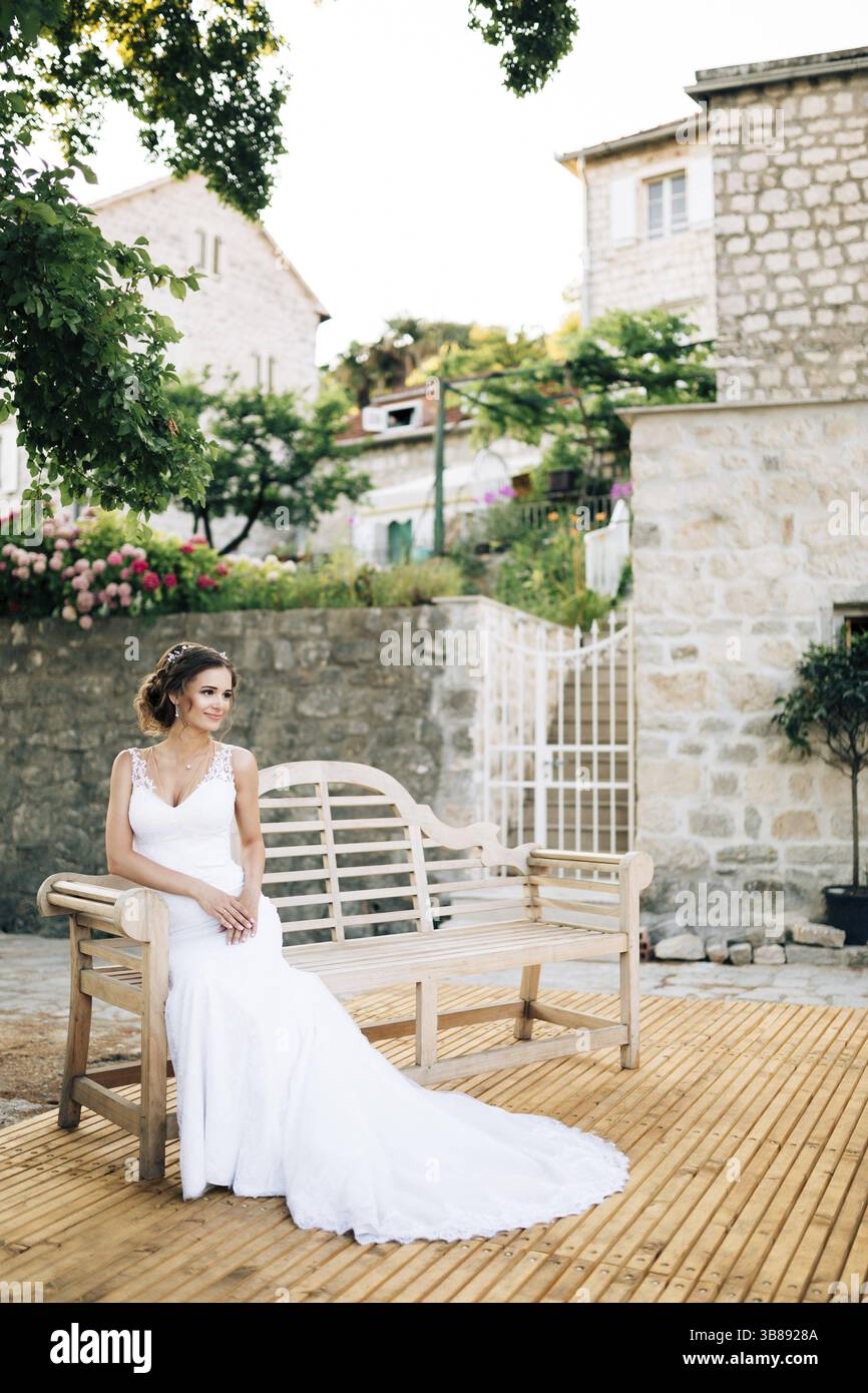 Kotor, Montenegro - 20.06.17: La sposa si trova su una panca di legno in un cortile accogliente vicino a case di mattoni bianchi. Perast Foto Stock