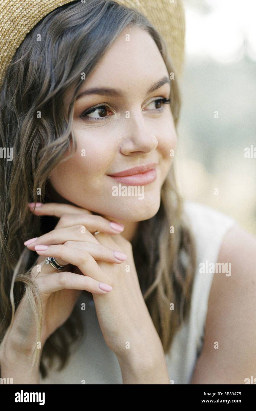 Donna sorridente in un cappello di paglia con le mani agganciate sotto il mento. Foto Stock