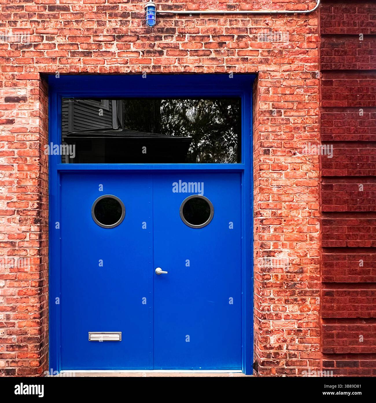 Le doppie porte blu vivo con finestre a oblò poste su una facciata in mattoni rossi creano un audace contrasto geometrico in un paesaggio urbano di Chicago Foto Stock