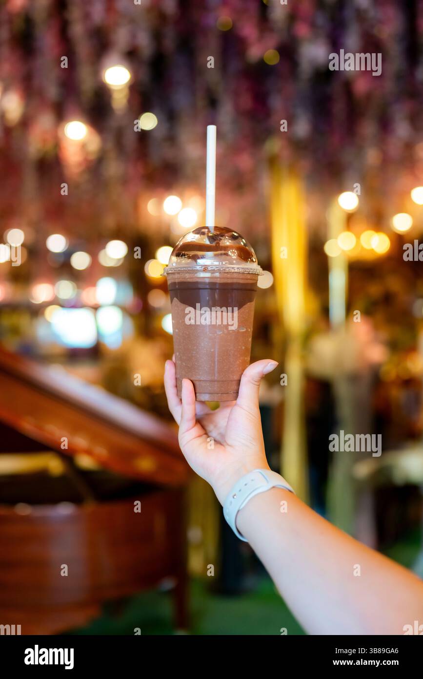 Una mano regge una bevanda fredda al cioccolato condita con sciroppo all'interno del caffè del Museo del cioccolato di Cartagena, Colombia, circondato da un'illuminazione elegante Foto Stock