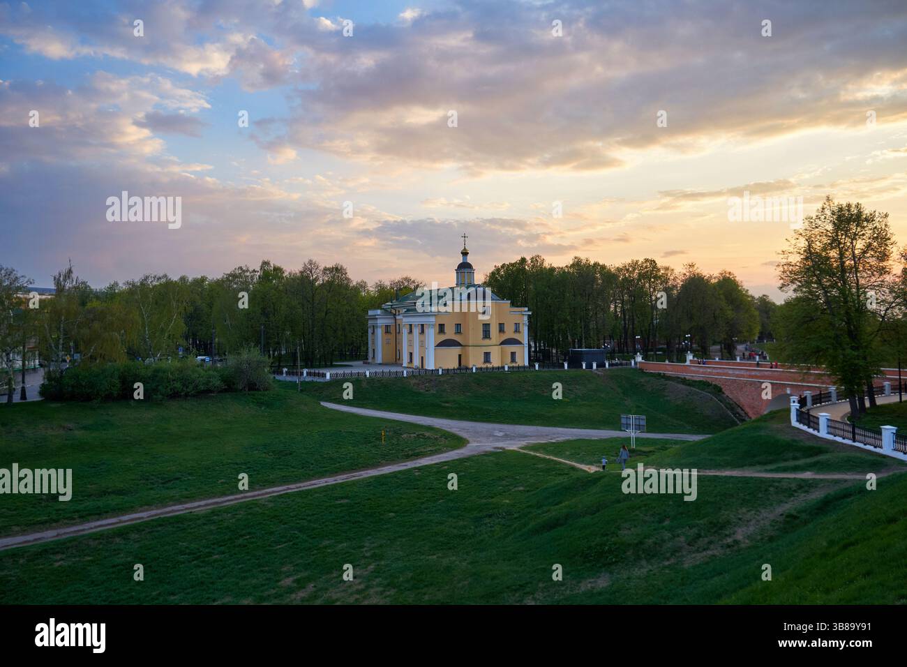 Parco cittadino e chiesa gialla al tramonto in primavera Foto Stock