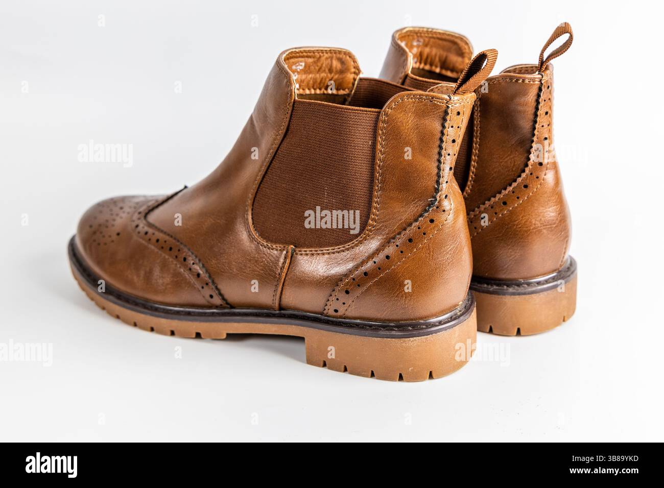 Un paio di stivali Chelsea marroni in pelle con dettagli in brogue e suola in gomma su sfondo bianco. Foto Stock