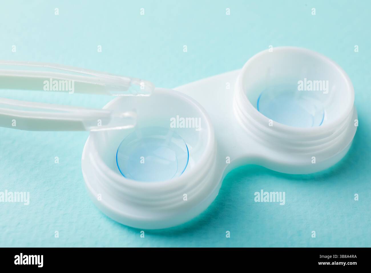 Lenti a contatto in astuccio e pinzette su sfondo turchese, primo piano Foto Stock