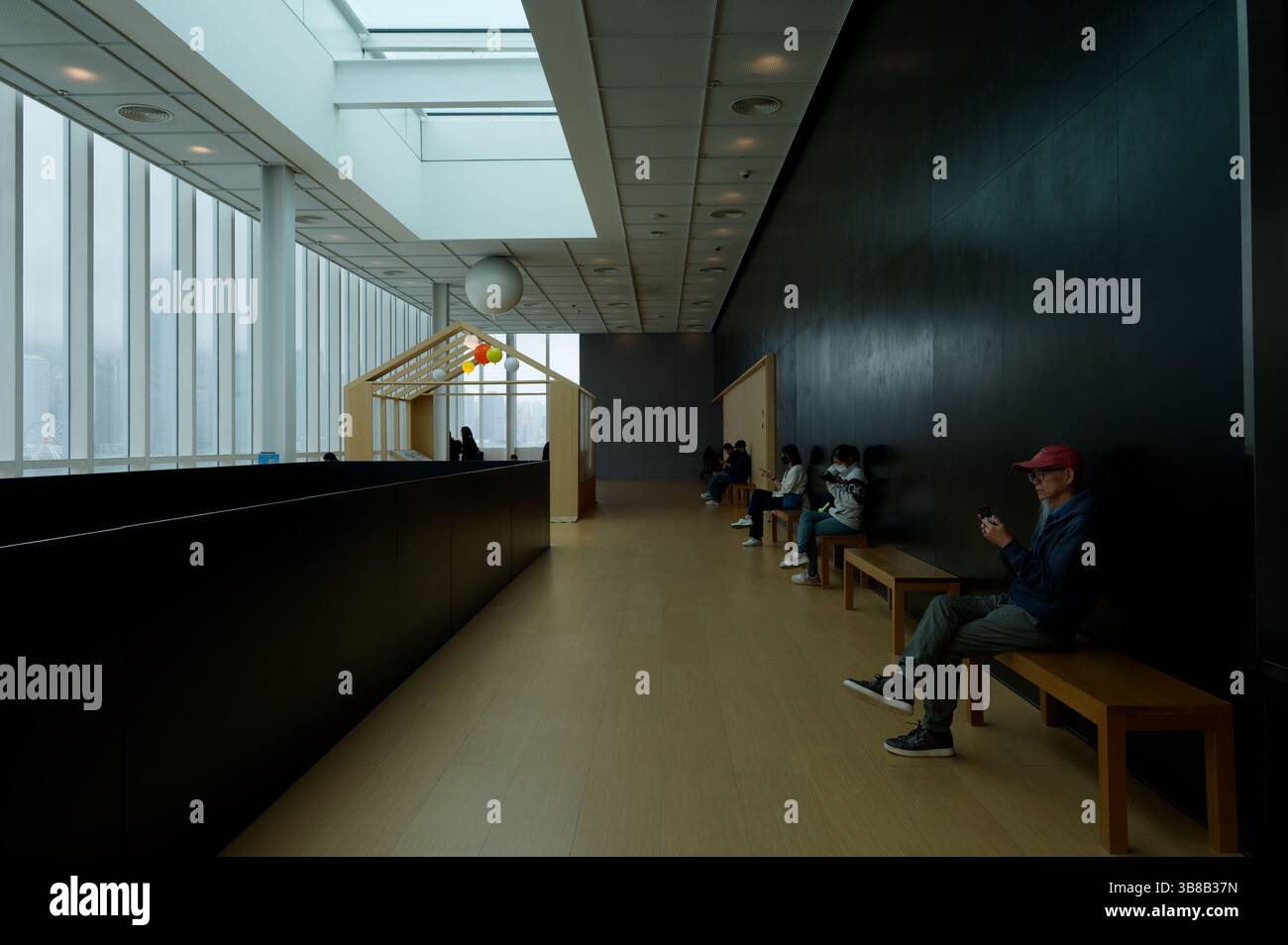 Momenti tranquilli all'HKMoA, mentre i visitatori si siedono nel silenzio contemplativo contro un muro buio, alcuni immersi nei loro telefoni Foto Stock