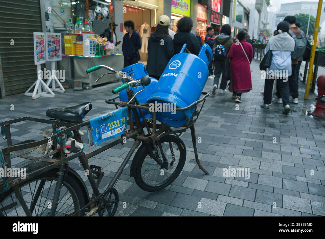 Bombole di gas blu bilanciate su una bicicletta usurata in mezzo a una strada trafficata di Hong Kong Foto Stock