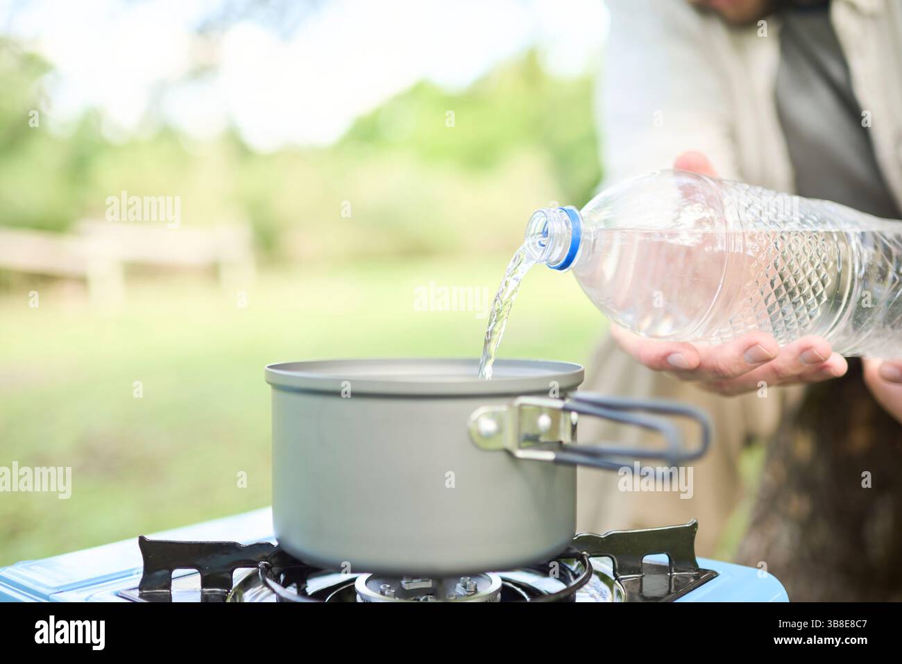 Persona irriconoscibile che versa acqua potabile in una pentola come parte del processo di cottura all'aperto, in una stufa a gas portatile, durante il campeggio. Selettivo Foto Stock