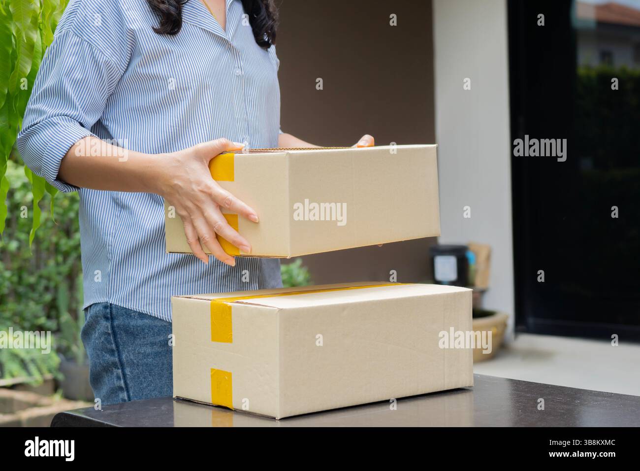 Donna asiatica in piedi e in possesso di grandi pacchi di cartone dopo aver ricevuto dal servizio di consegna a casa. Foto Stock