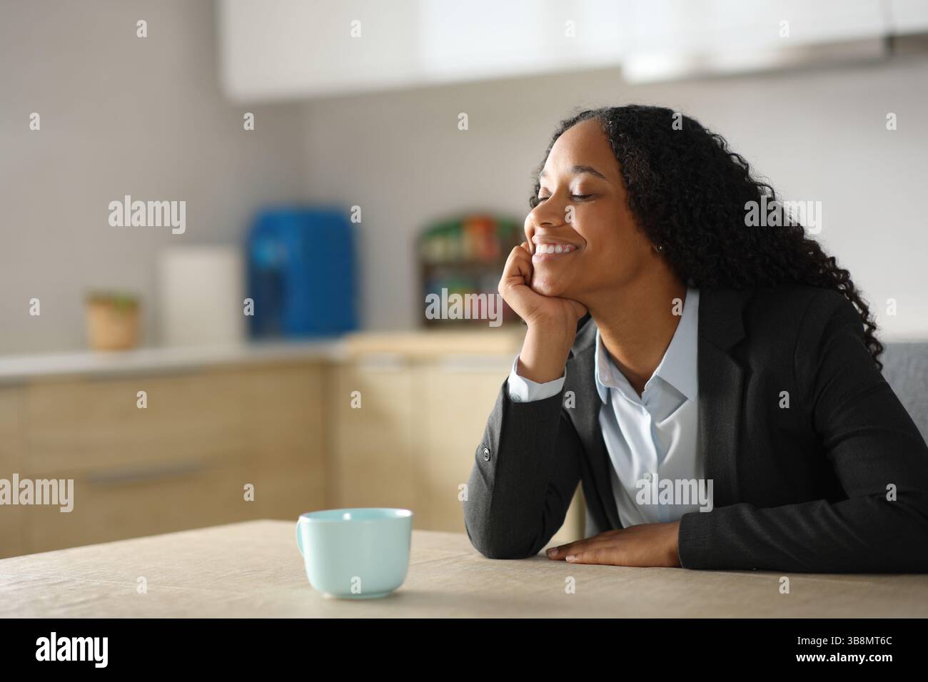 Buon dirigente nero che si rilassa seduto nella cucina di casa Foto Stock