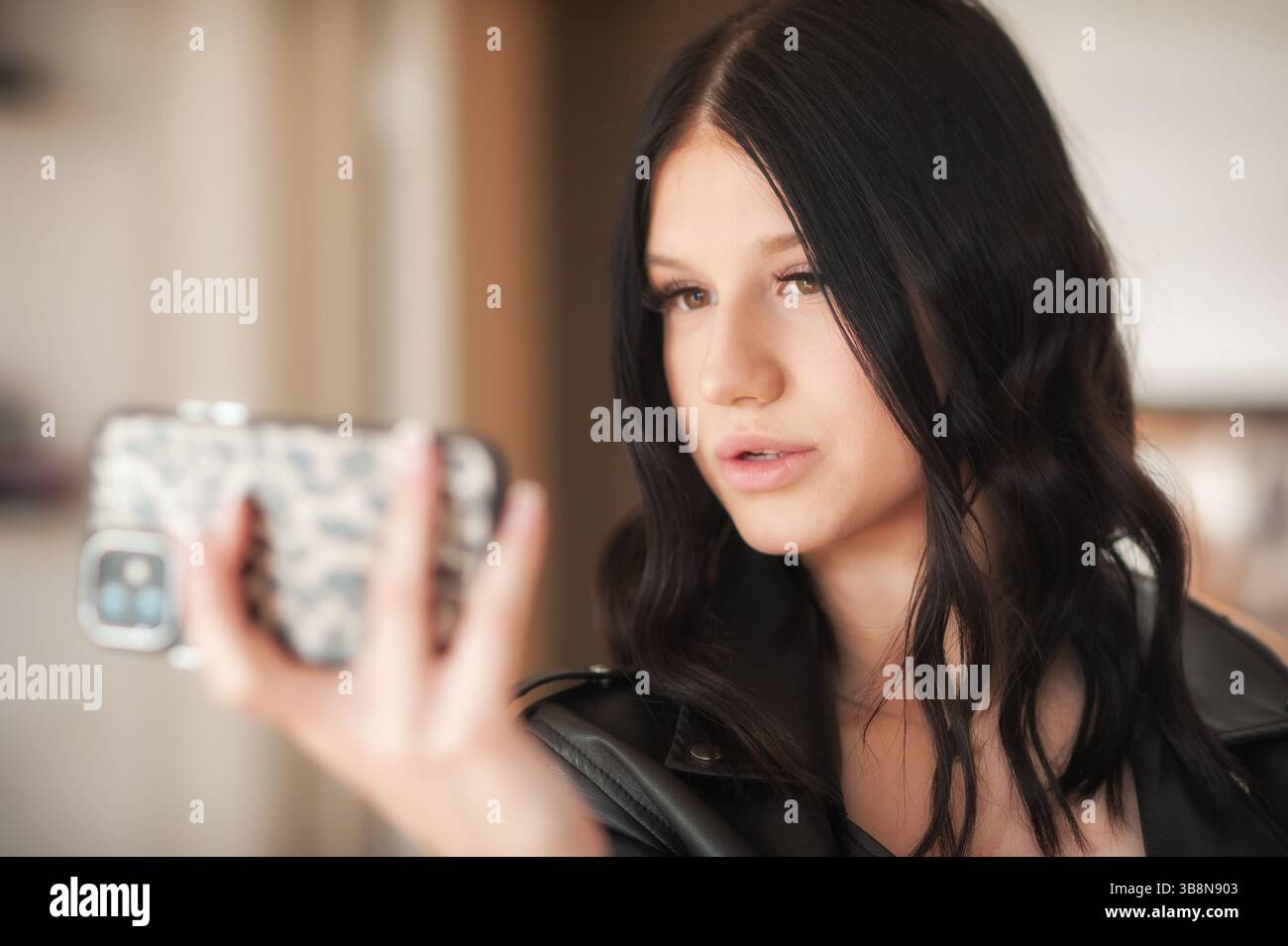 Una ragazza alla moda dai capelli ondulati cattura il suo look elegante sui social media, indossando un outfit chic. L'ambiente moderno migliora la sua influenza Foto Stock