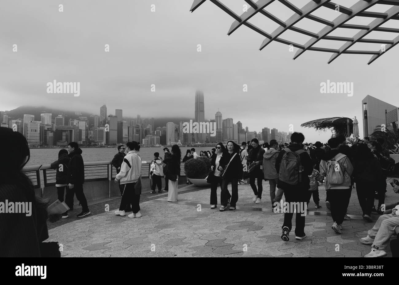 La folla si raduna lungo il Victoria Harbour mentre lo skyline di Hong Kong ricoperto di nebbia si incammina sull'acqua Foto Stock