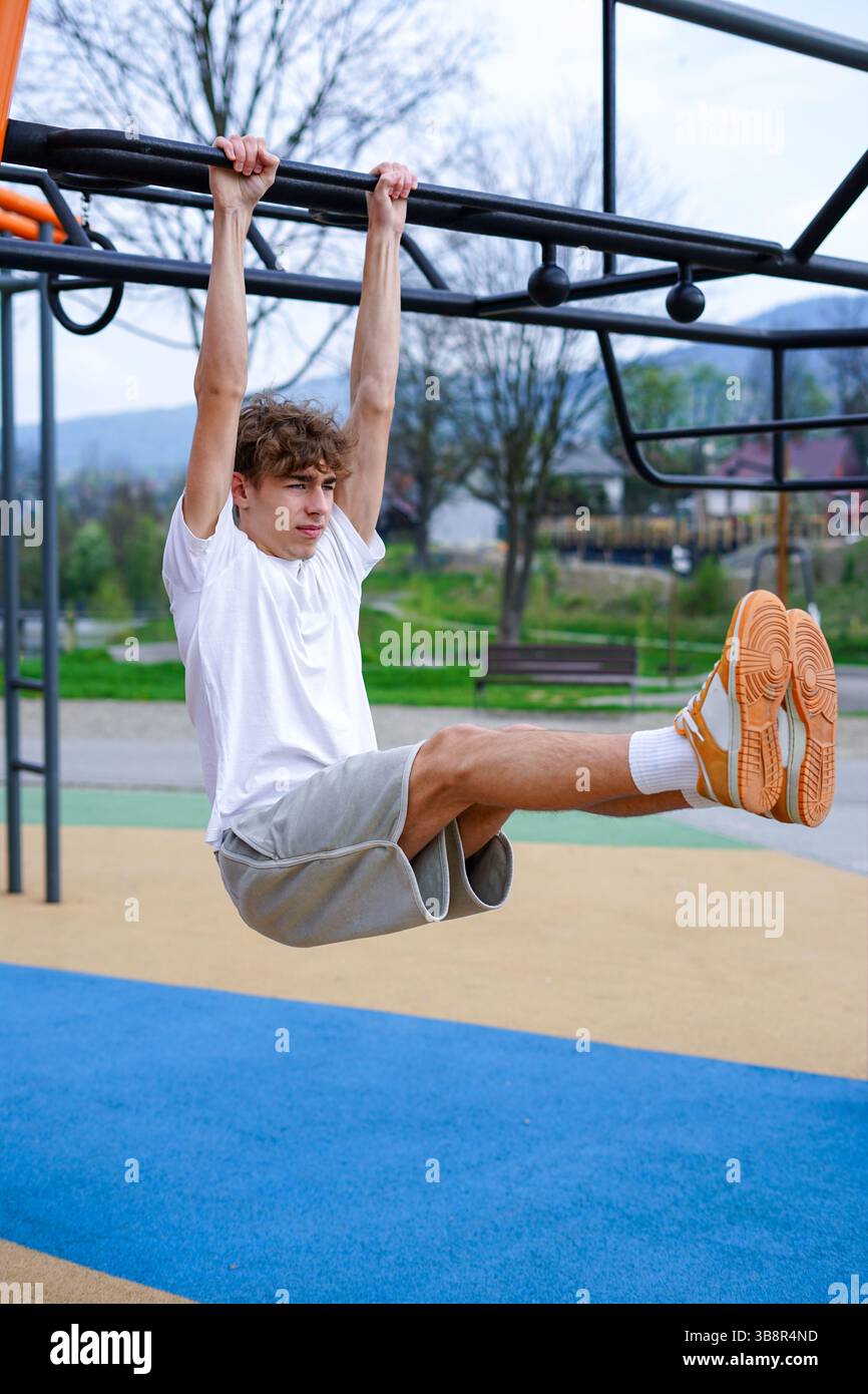 L'atletico esegue il sollevamento delle gambe appese su un bar fitness all'aperto Foto Stock