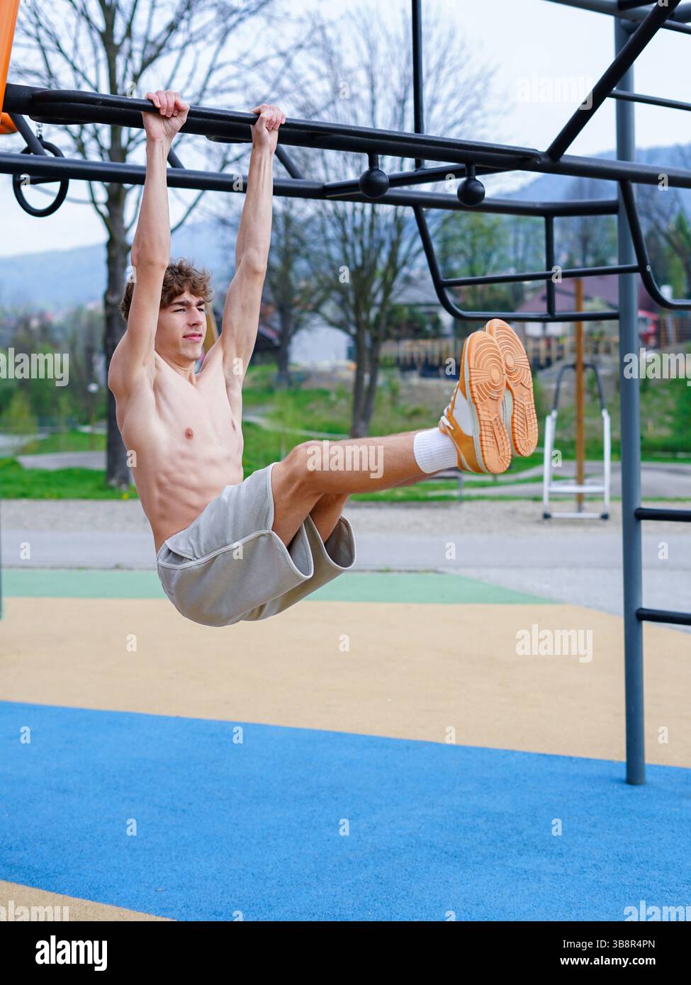 L'atletico esegue il sollevamento delle gambe appese su un bar fitness all'aperto Foto Stock
