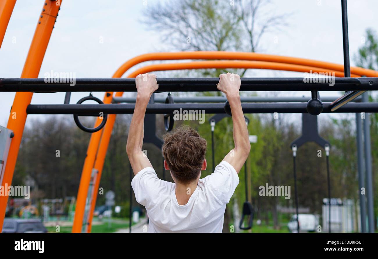 Il giovane allena la resistenza della parte superiore del corpo con pull-up su una struttura fitness all'aperto Foto Stock