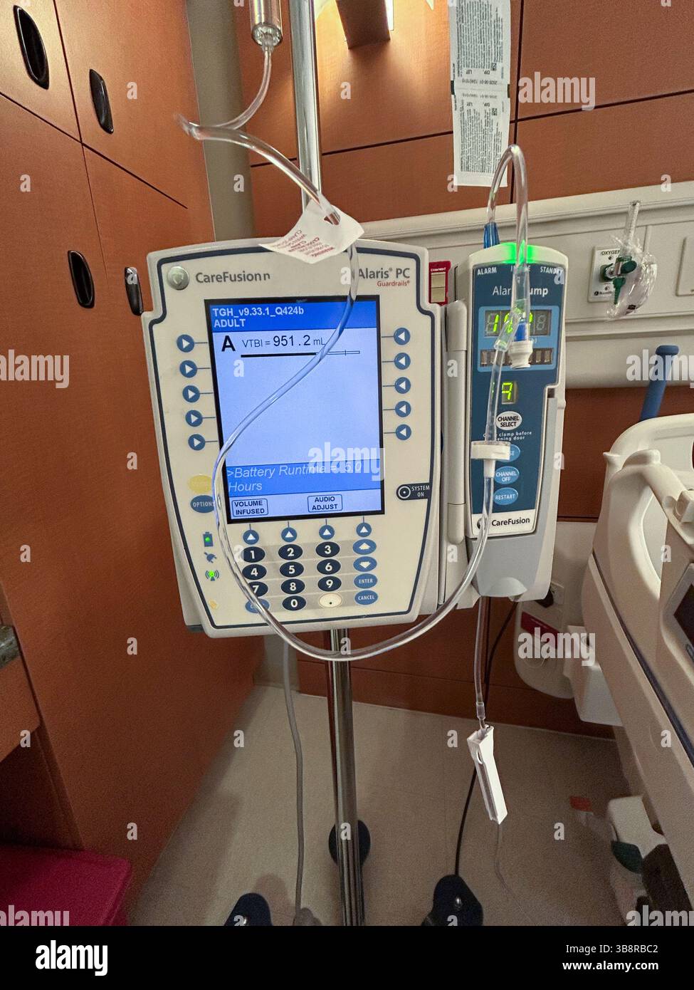 Una pompa di infusione medica in una stanza ospedaliera che fornisce fluidi e farmaci a un paziente. Foto Stock