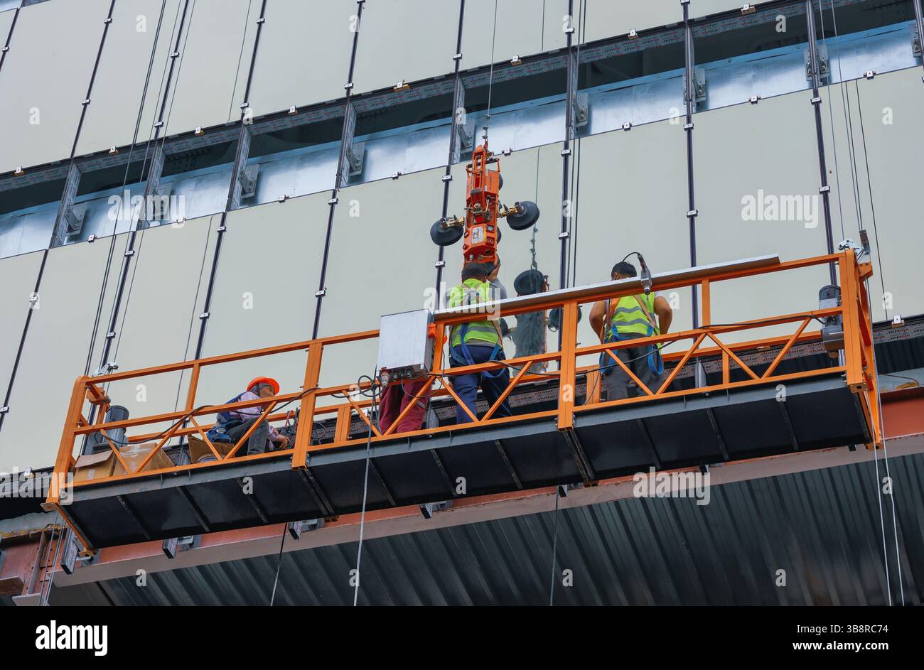 Almaty, Kazakistan - 29 aprile 2025: I lavoratori in una culla di costruzione installano una finestra con un martinetto di vetro. Lavori di facciata Foto Stock