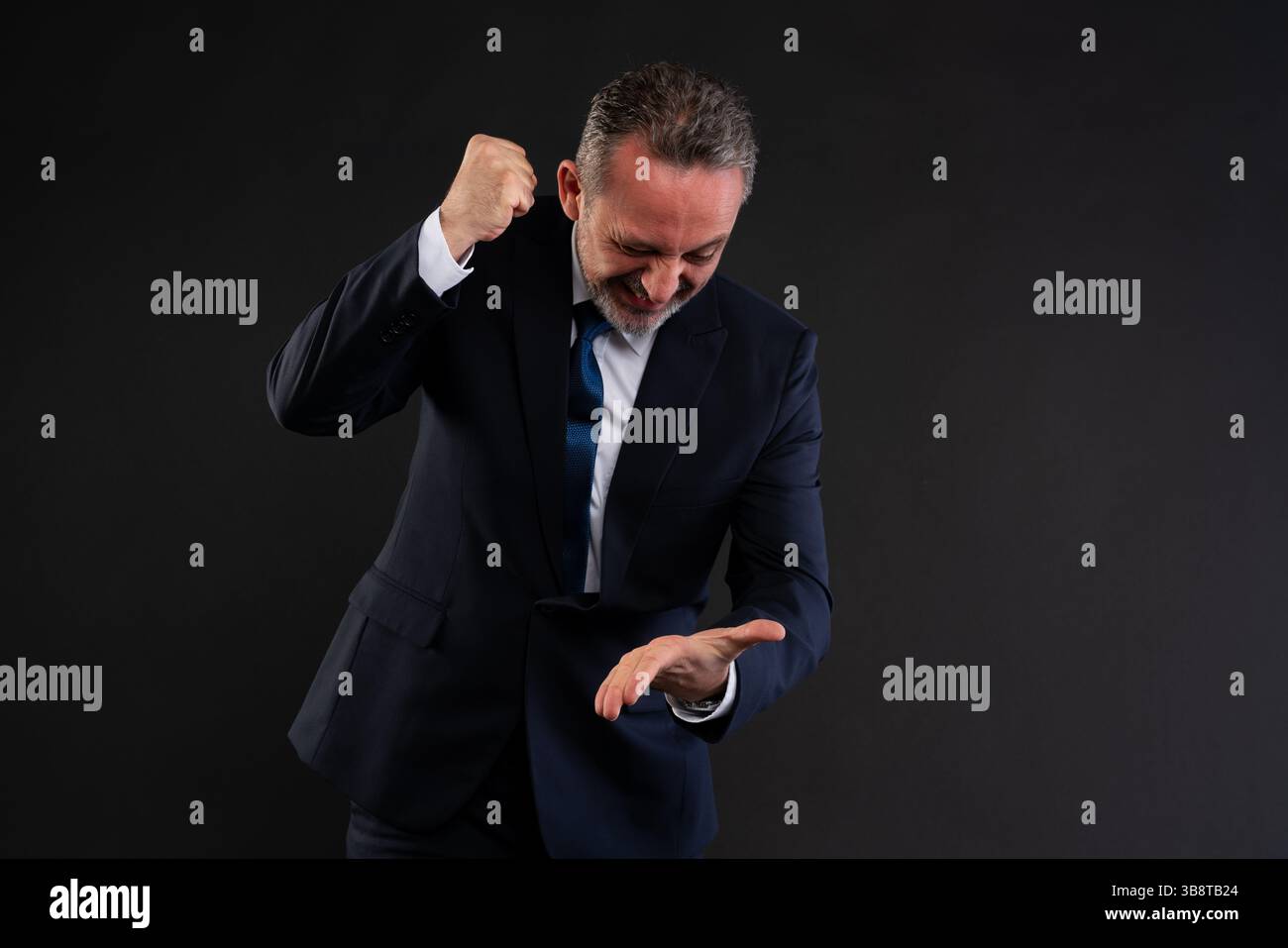 Uomo d'affari in tuta formale che sbatte con rabbia il pugno nel palmo dell'altra mano, esprimendo frustrazione, fallimento o intensa emozione. Ripresa in studio Foto Stock