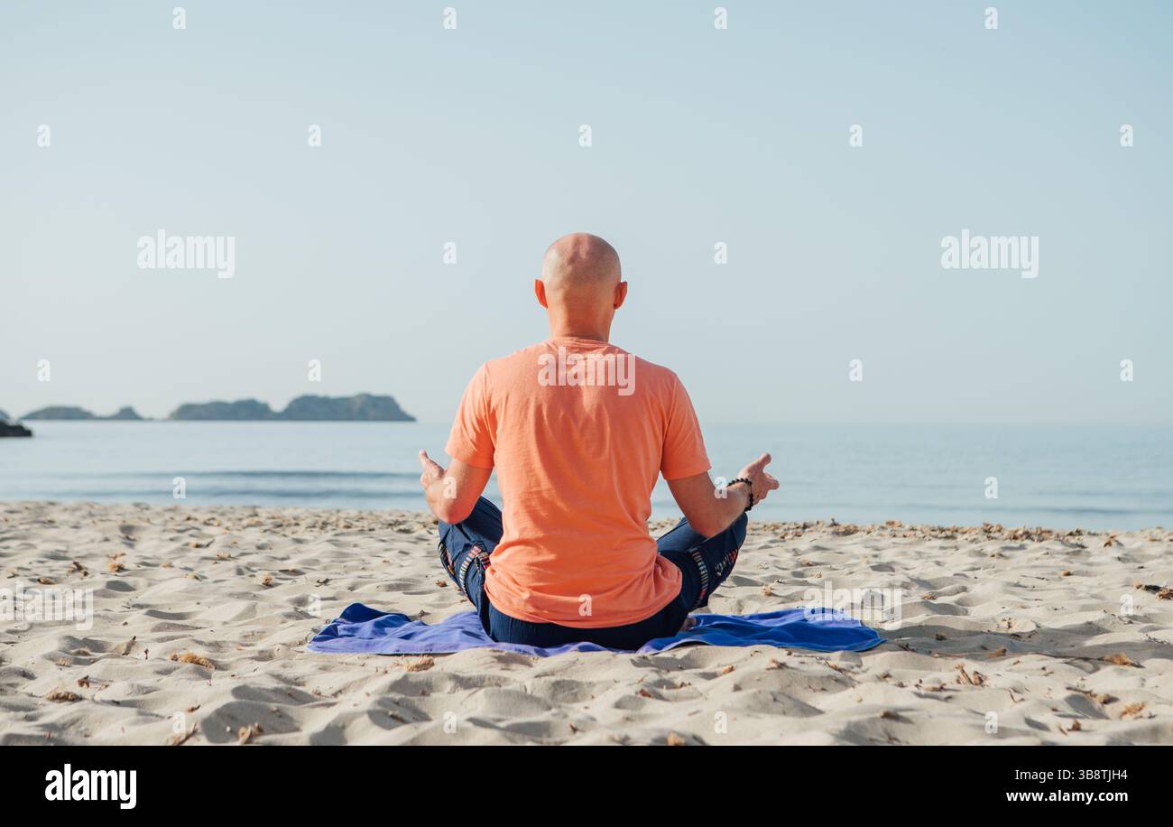 Uomo calmo seduto in posizione di loto, facendo esercizi di respirazione profonda di yoga e meditando nelle prime ore del mattino sulla spiaggia sabbiosa con onde calme del mare. Med Foto Stock