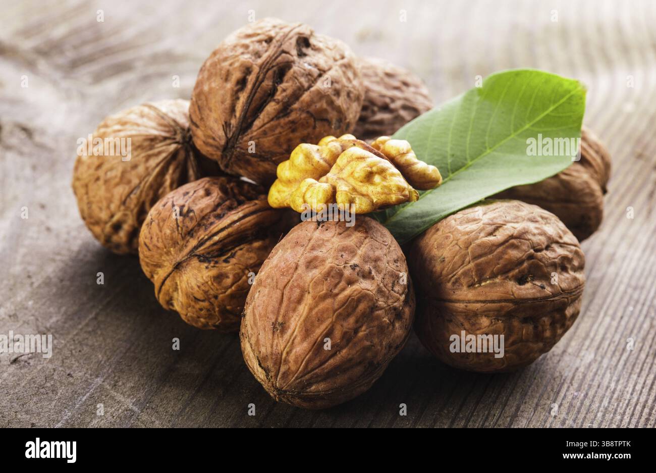 Noci comuni con guscio e foglia verde sul tavolo di legno Foto Stock