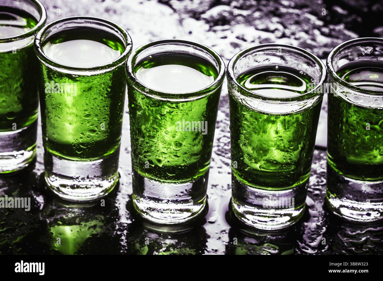 Bicchieri di vodka. Molti alcolici bevono in una consistenza di fila. Sfondo della festa nel fine settimana. Riflesso della superficie del wet bar verde. Gocce di liquore retroilluminate. Foto Stock
