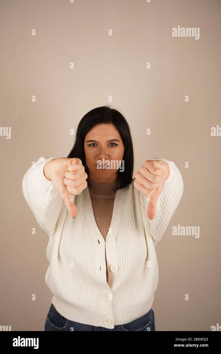 Donna seria che mostra un doppio gesto verso il basso, esprimendo delusione. La sua espressione focalizzata enfatizza l'emozione dell'antipatia. Un messaggio chiaro Foto Stock