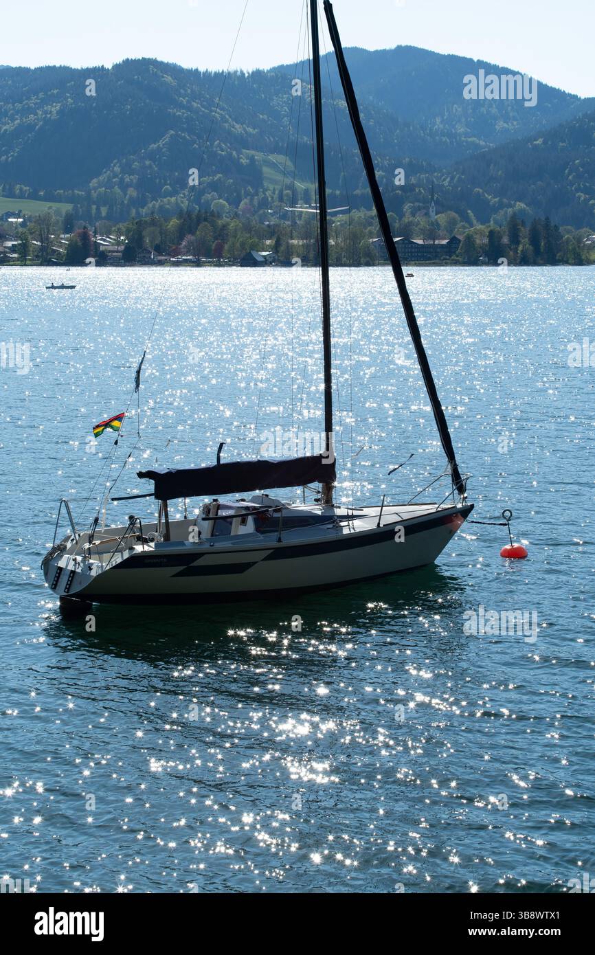 Barca a vela bianco-nero ancorata in acque scintillanti con boa arancione e gattino svolazzante, serenità a dorso di montagna sotto il cielo blu, calma nautica. Foto Stock