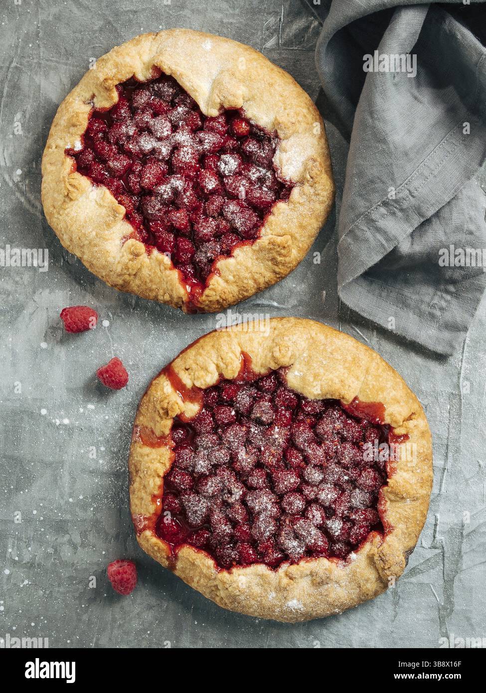 Due perfette galette di lamponi. Deliziosa crostata rustica fatta in casa con lamponi freschi o congelati, sfondo grigio. Belle galette rotonde con raspa Foto Stock