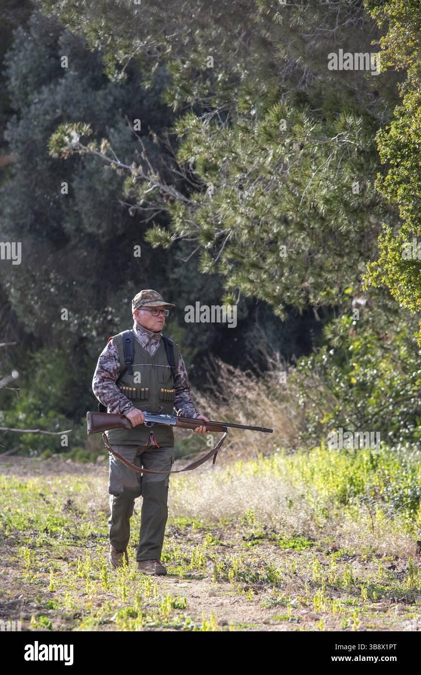 Cacciatore che cammina attraverso fitti boschi, porta con sé un fucile mentre ama una caccia diurna nei grandi spazi aperti, abbracciando lo sport della caccia a Sant per Foto Stock