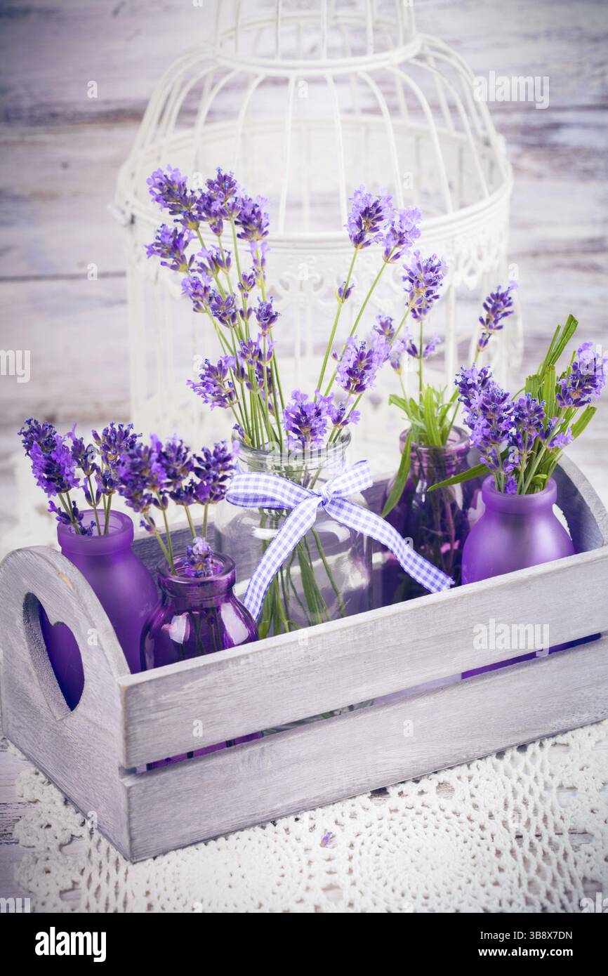 Lavanda in bottiglia, stile provance decor, scatola di legno e gabbia per uccelli su tovaglia a crochet Foto Stock