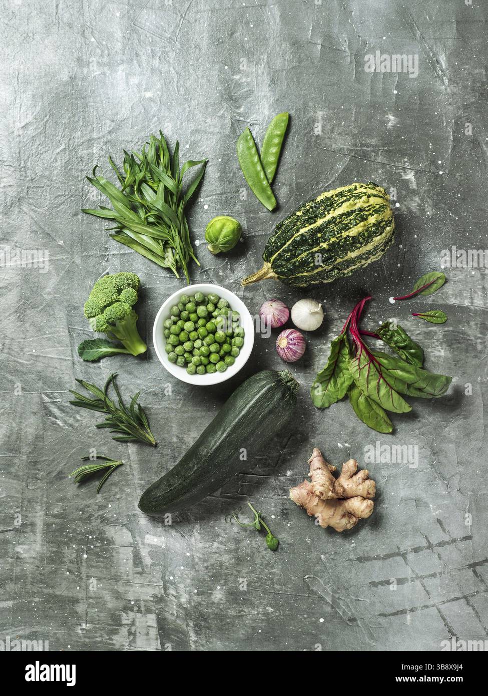 Verdure verdi ed erbe su sfondo grigio, top view.Still life con piselli verdi, zucchine, fagioli-pod, zucca, zenzero, aglio, broccoli, dragoncello, b Foto Stock