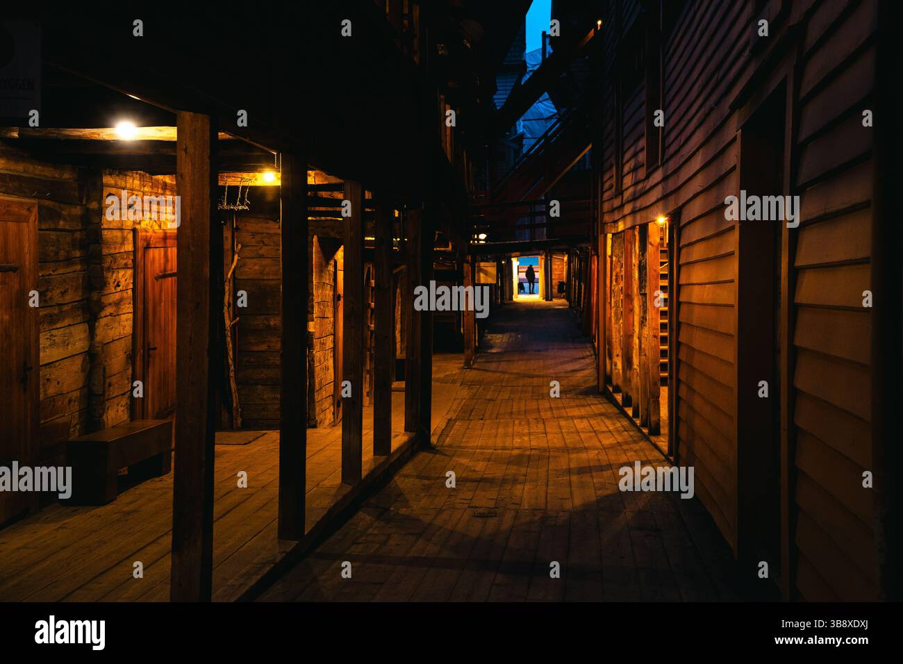 Suggestive scene notturne da Bryggen Wharf a Bergen, Norvegia, che mostrano negozi accoglienti, vicoli illuminati ed edifici storici in legno in caldi luci Foto Stock