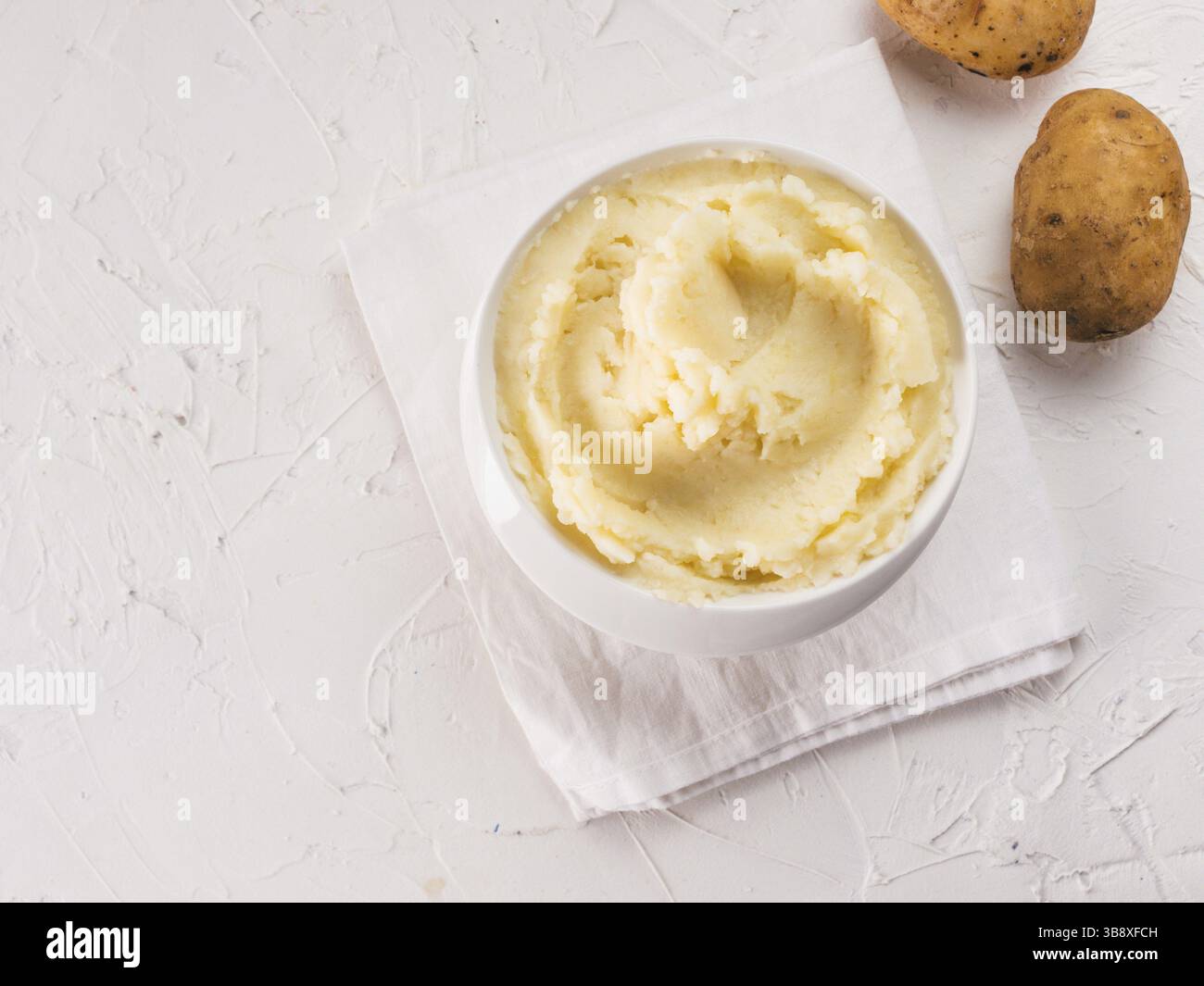 Purè di patate in un recipiente bianco con tovagliolo su sfondo bianco in cemento testurizzato. Vista dall'alto o disposizione piatta. Copia spazio Foto Stock