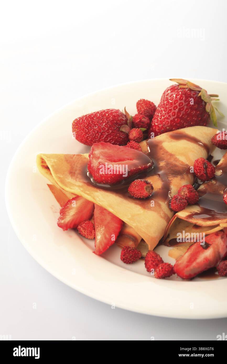Frittelle con differenti le fragole con lo sciroppo di cioccolato su bianco Foto Stock