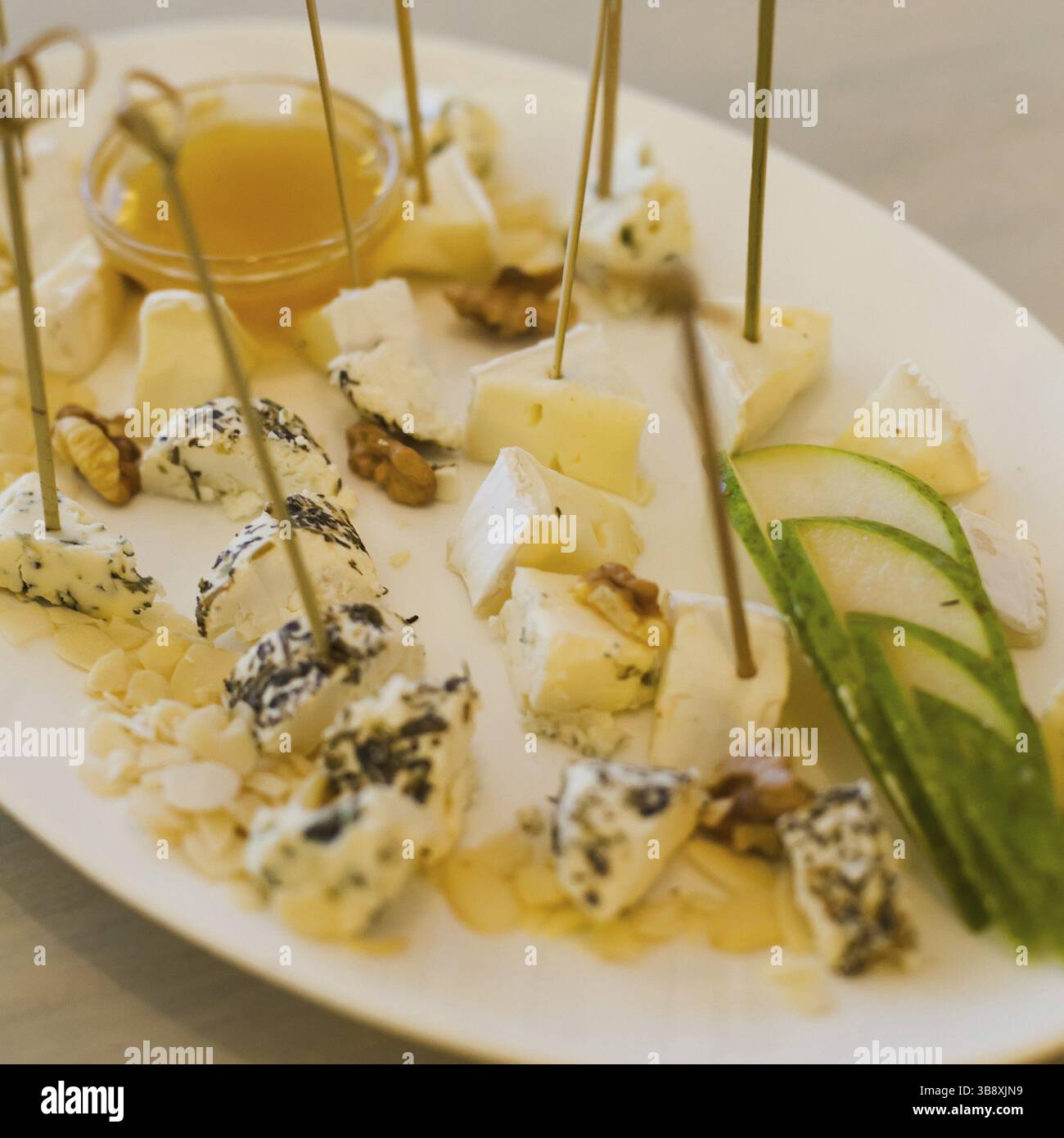 Piastra con diversi tipi di formaggi, miele, noci e pera Foto Stock