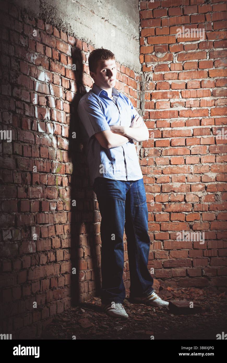 Uomo appoggiato su un muro di mattoni in una casa abbandonata incompiuta Foto Stock