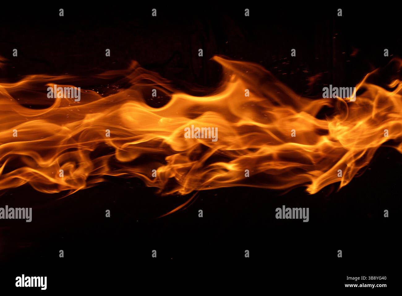 Le fiamme danzanti si estendono orizzontalmente su uno sfondo nero profondo, catturando la natura ipnotica ed eterea del fuoco in movimento. Foto Stock