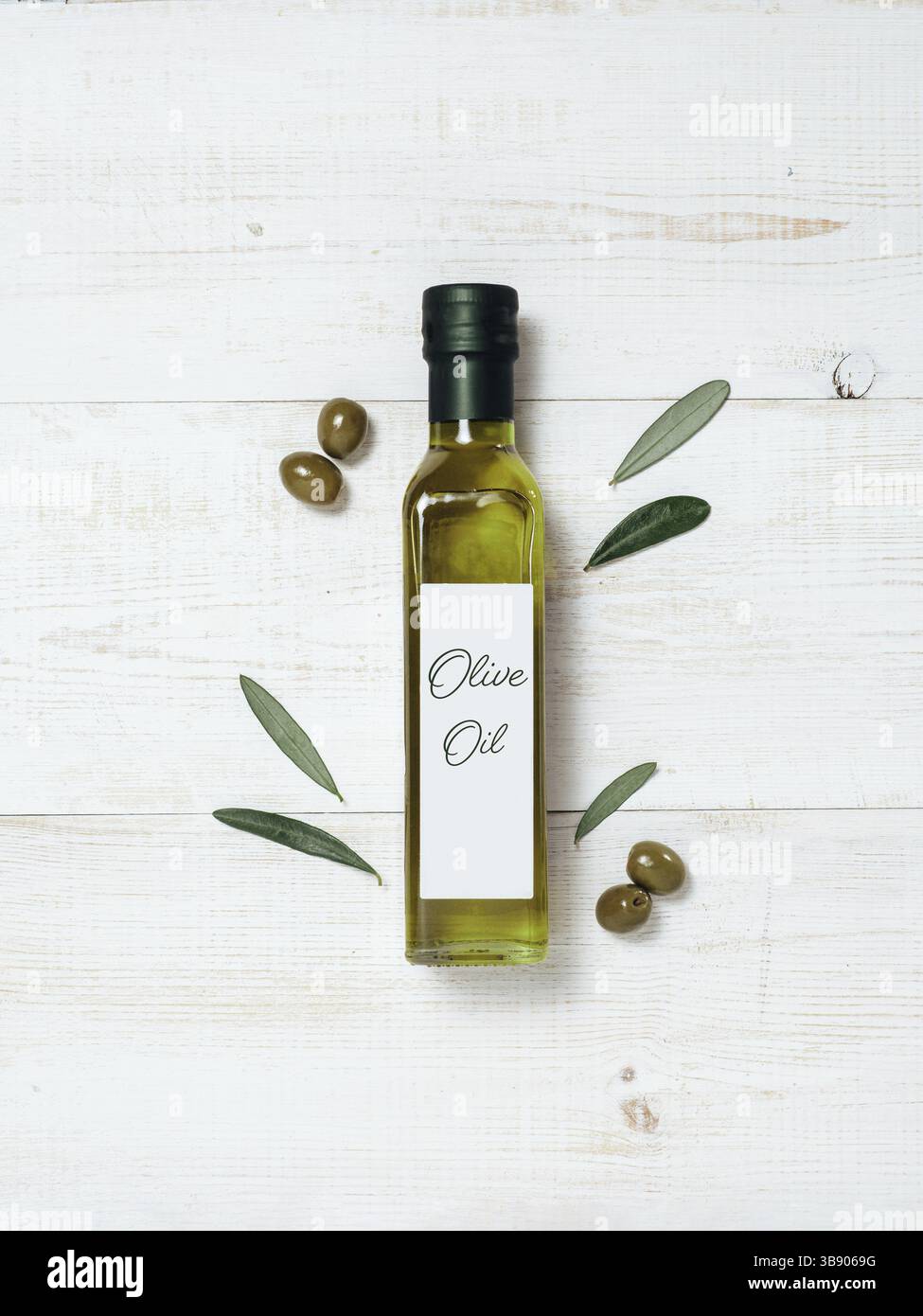 Modello della bottiglia di vetro dell'olio d'oliva. Vista dall'alto della bottiglia di vetro verde con olio extra vergine d'oliva su sfondo di legno bianco con olive verdi e gree fresco Foto Stock