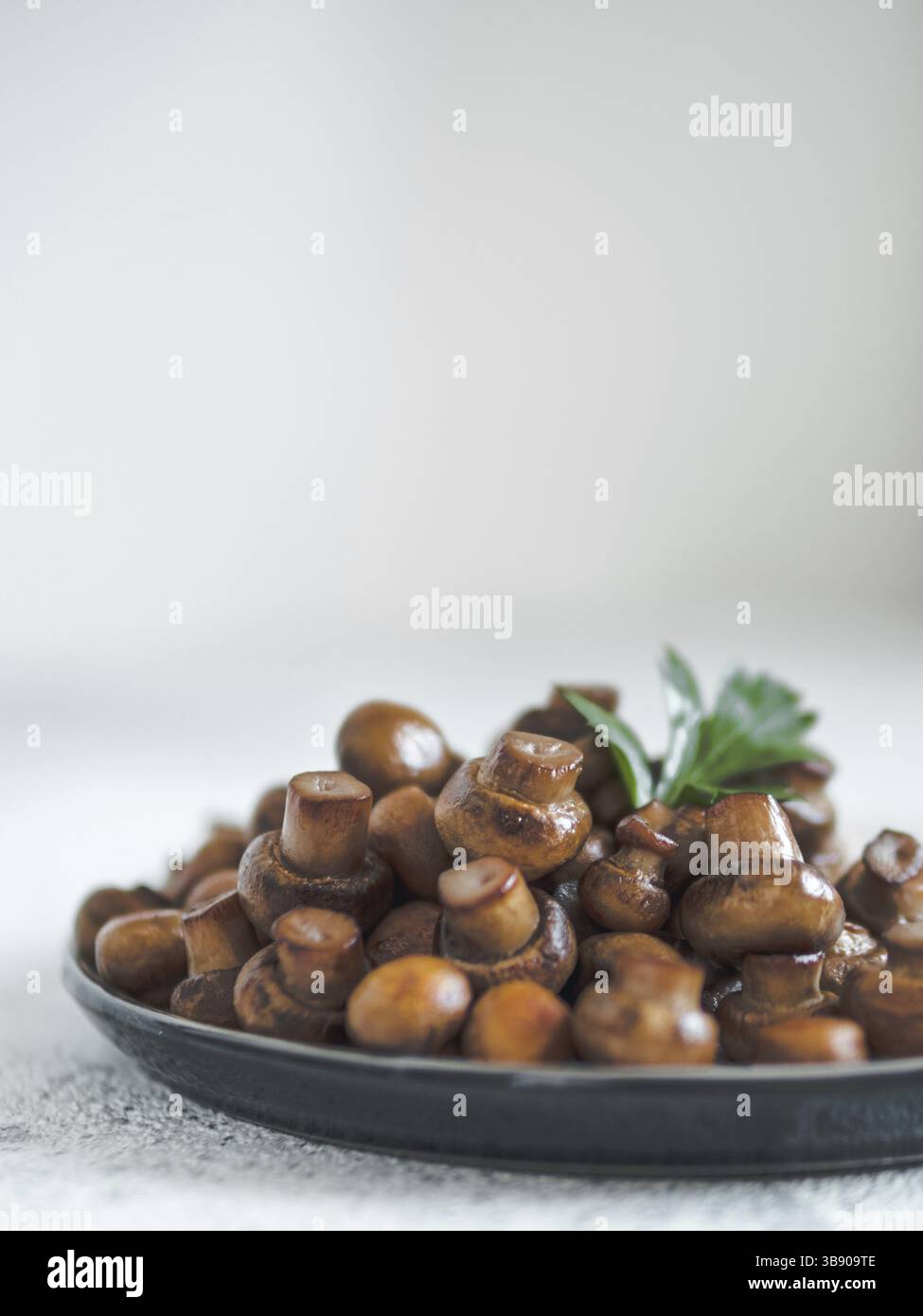 Mini champignons fritti pronti da mangiare su piastra con spazio per la copia. Perfetti mini funghi mucchio su piastra su fondo grigio cemento. Luce naturale. Ver Foto Stock