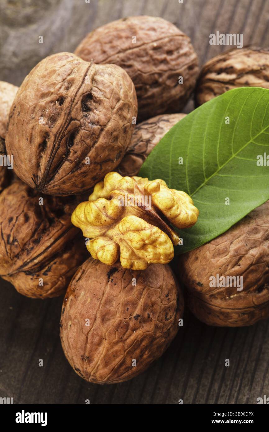 Noci comuni con guscio e foglia verde sul tavolo di legno Foto Stock