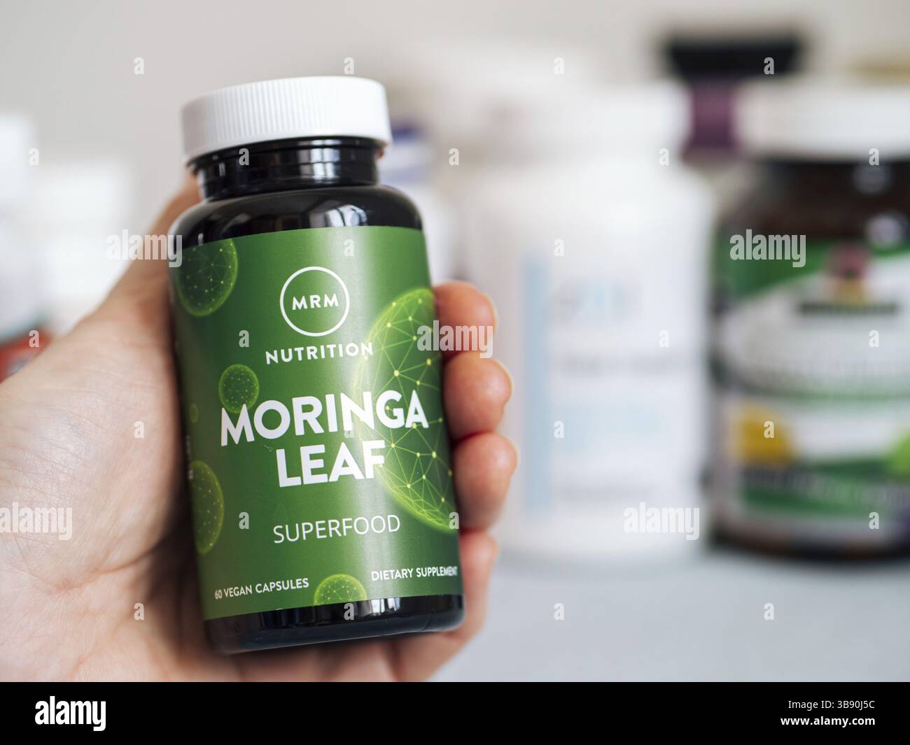 Mosca, Russia - 09 marzo 2021: Vaso con capsule di Moringa Leaf di MRM in mano femminile e altri integratori alimentari in background sfocato. Moringa Foto Stock