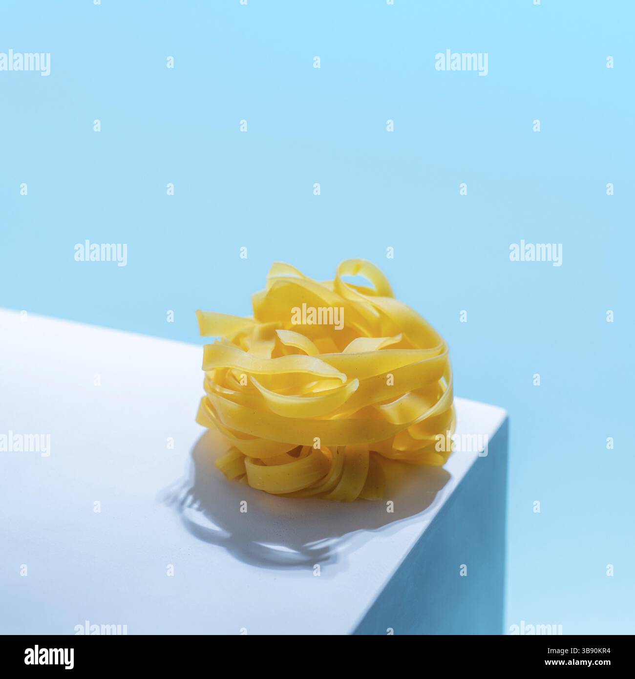 Pasta art. Tagliatelle su piedistallo blu pastello su sfondo blu in luce dura. Un tocco creativo di pasta noodle. Design creativo per menu di ital Foto Stock