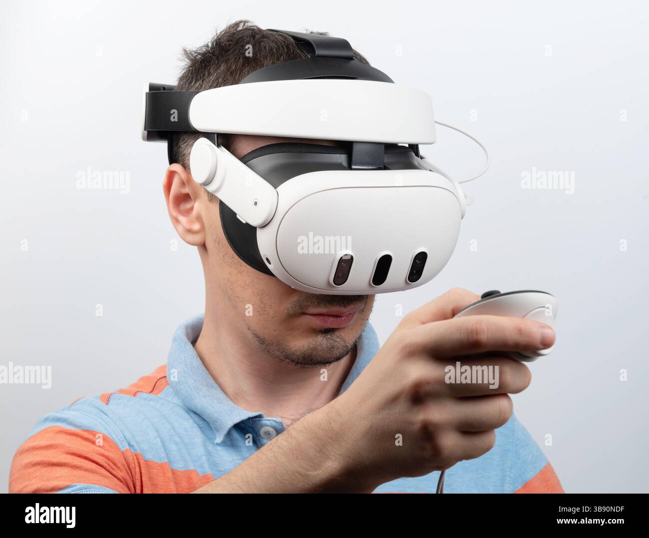 Impegnato in un'esperienza virtuale immersiva, l'uomo indossa il visore VR e tiene il controller a fuoco. Foto Stock