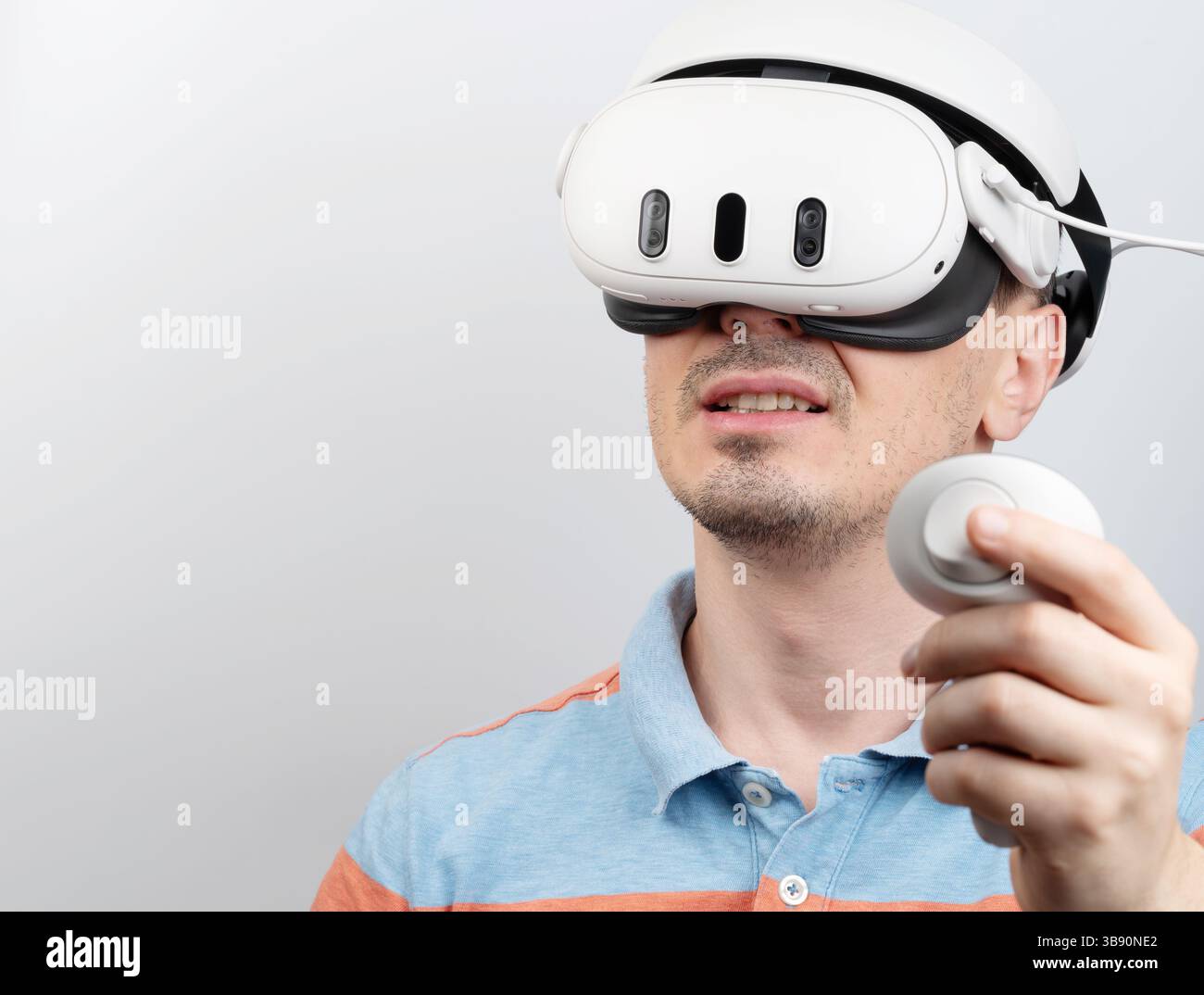 Impegnato in un'esperienza virtuale immersiva, l'uomo indossa il visore VR e tiene il controller a fuoco. Foto Stock