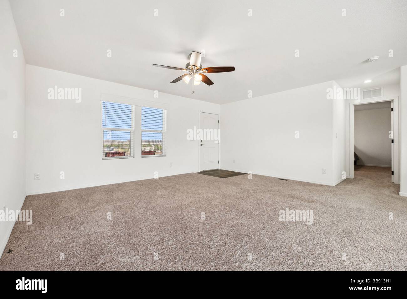 Un soggiorno vuoto con ventilatore a soffitto sopra, abbinato a due finestre che contribuiscono a creare l'atmosfera generale della camera Foto Stock