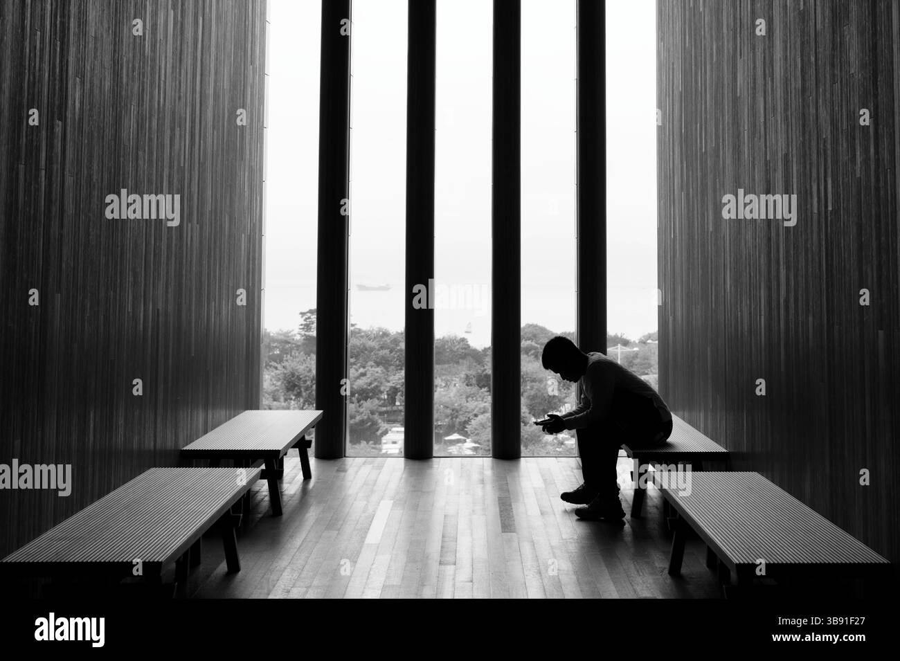 Silhouette contemplativa incorniciata da luce naturale all'interno del corridoio minimalista del Museo M+ Foto Stock