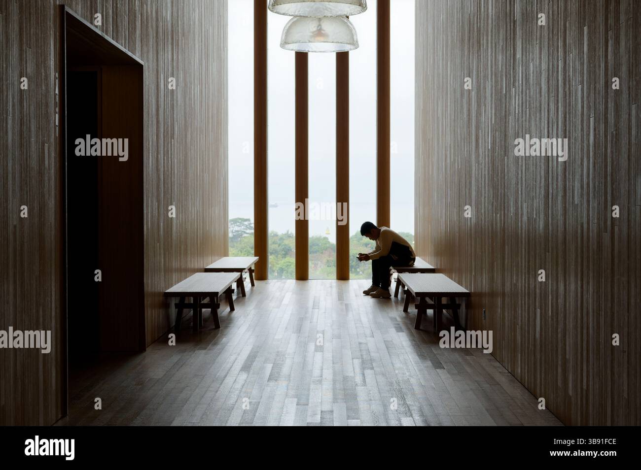 Riflesso in un corridoio minimalista all'interno del Museo M+, incorniciato da luce naturale e da una lontana vista verde Foto Stock