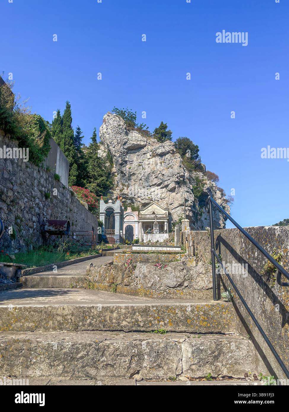 Eze, Francia - 9 luglio 2024: Chiesa, cimitero Église Notre-Dame-de-l'Assomption, le scale fino ad esso sotto il cielo blu e rocce bianco-grigie sul retro Foto Stock