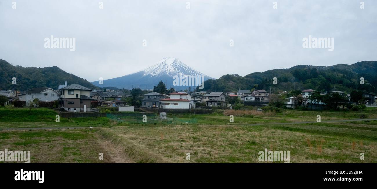 Vista panoramica del monte fuji che torreggia su case e campi verdi, mostrando l'armonia della natura e della vita urbana in giappone Foto Stock