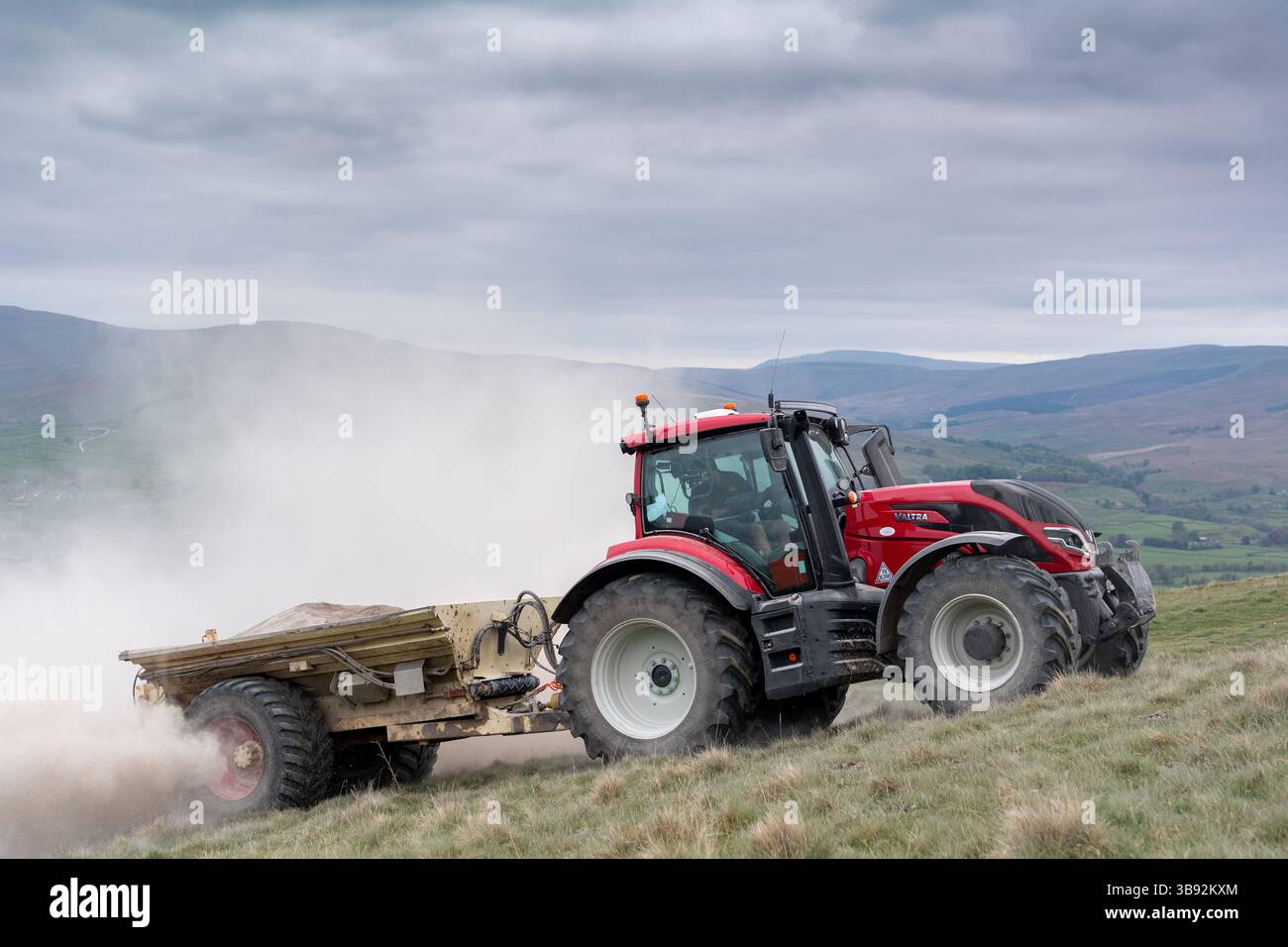 Appaltatore agricolo, alla guida di un trattore Valtra rosso, spalmando calce su un ripido pascolo per migliorare il pH del terreno e la qualità del terreno. Wensley Foto Stock