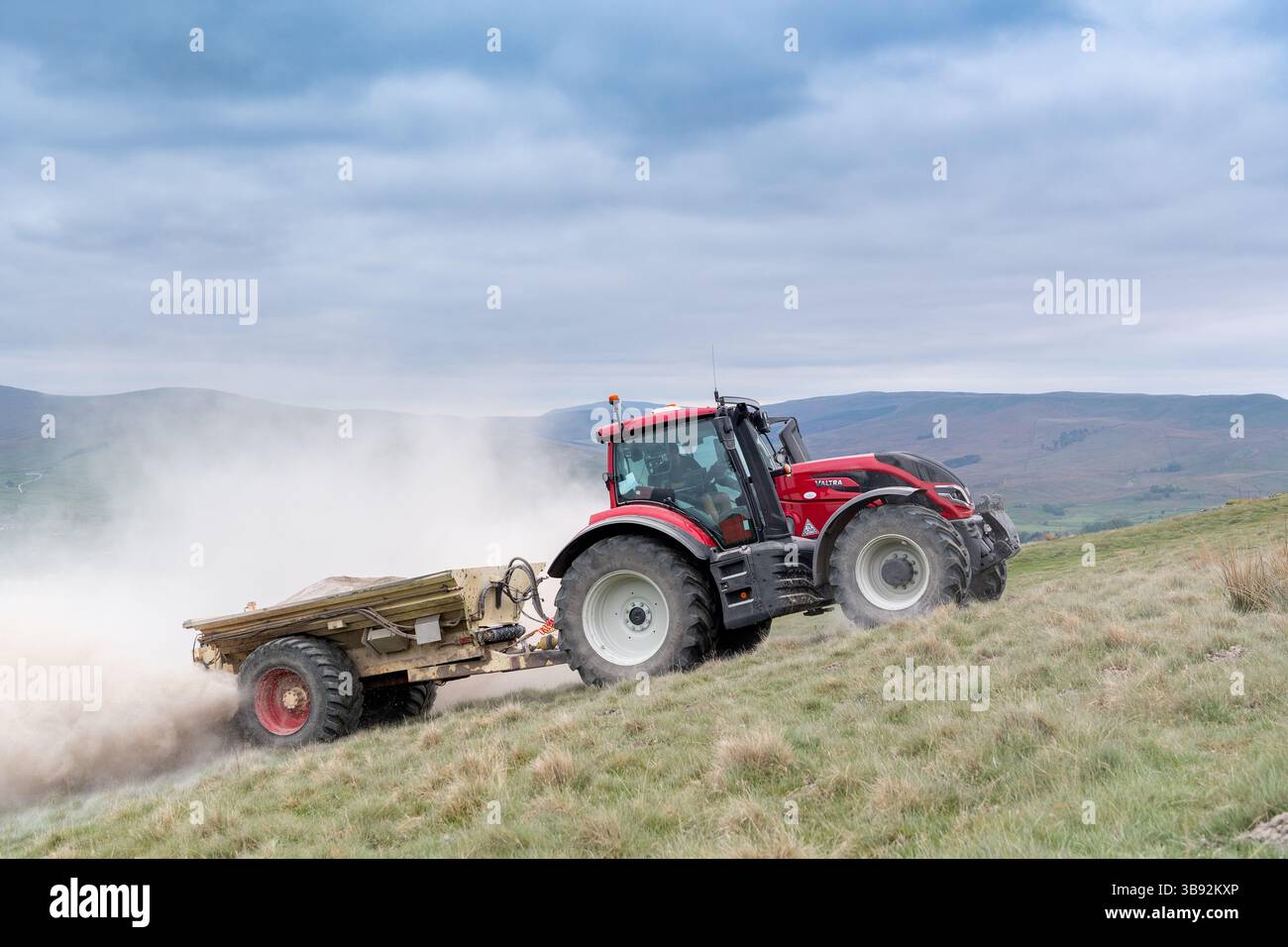 Appaltatore agricolo, alla guida di un trattore Valtra rosso, spalmando calce su un ripido pascolo per migliorare il pH del terreno e la qualità del terreno. Wensley Foto Stock