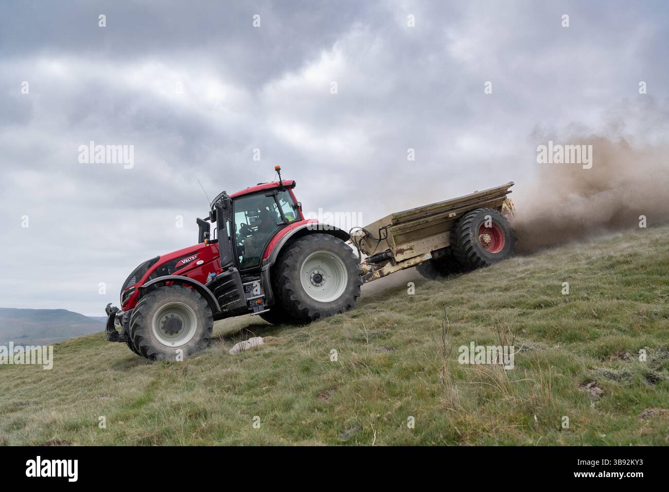 Appaltatore agricolo, alla guida di un trattore Valtra rosso, spalmando calce su un ripido pascolo per migliorare il pH del terreno e la qualità del terreno. Wensley Foto Stock